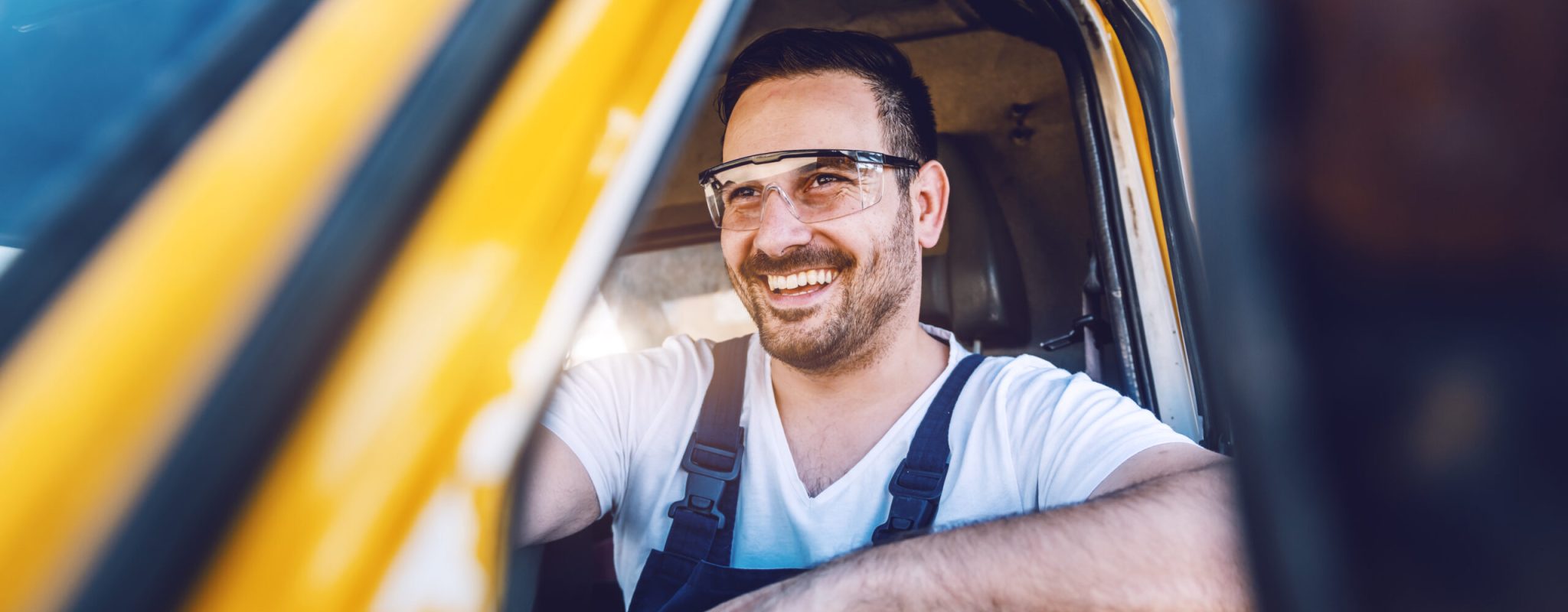 Smiling handsome unshaven worker driving vehicle on construction site.